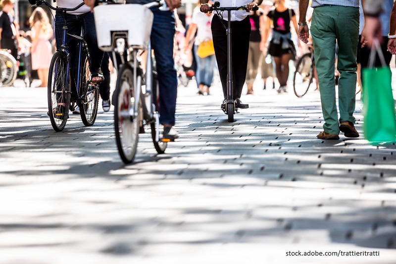 Stadtszene, in der sich die Menschen unterschiedlich fortbewegen, auf Fahrrädern und E-Scootern.