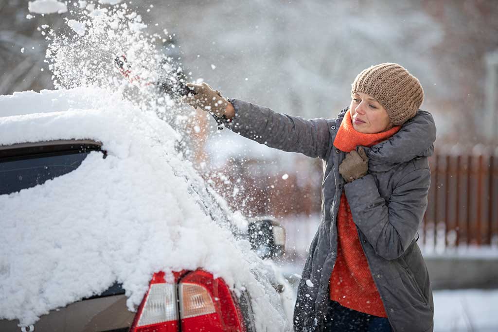 Autofahren im Winter nur mit guter Sicht: Eine Frau kratzt die Scheiben Ihres Autos frei