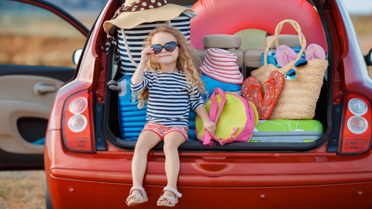 Startklar für den Urlaub mit dem eigenen Auto: Kind sitzt im Kofferraum eines vollbepackten Autos