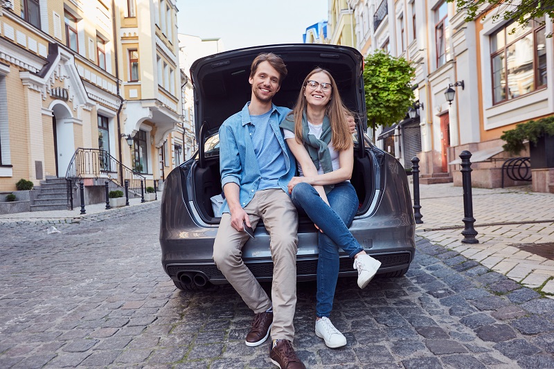 Junges Paar sitzt im Kofferraum seines Autos.