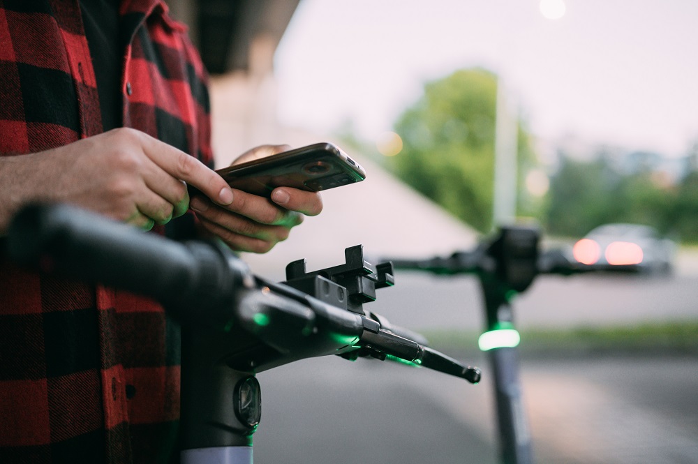 Mann mit Mobiltelefon und E-Scooter