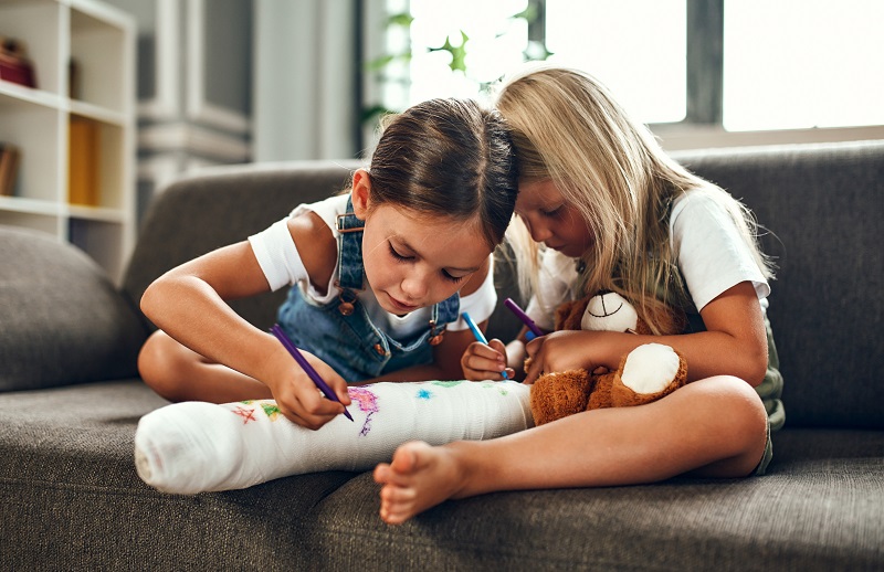 Zwei Schwestern, die auf den Gips des gebrochenen Beines der Schwester schreiben