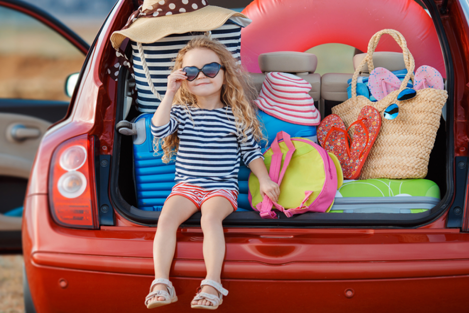 Startklar für den Urlaub mit dem eigenen Auto: Kind sitzt im Kofferraum eines vollbepackten Autos